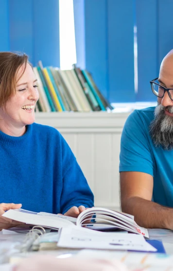 Two students in a Gaelic language class laughing while studying, with a Gaelic-English dictionary open on the desk. Two students in a Gaelic language class laughing while studying, with a Gaelic-English dictionary open on the desk.